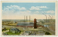 Color postcard showing the sprawling campus of a lumber mill, with a red two-story structure and silo in the middle ground and the horizon and sky in the background.